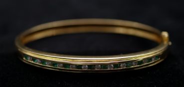 An 18 carat yellow gold, emerald and diamond bangle. Set with thirteen round mixed cut emeralds with