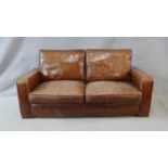 A contemporary vintage style sofa in tan leather upholstery on block platform supports. H.75 W.183