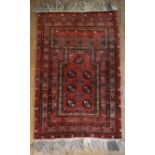 An Eastern prayer rug with repeating gul motifs on burgundy ground with stylised floral multi