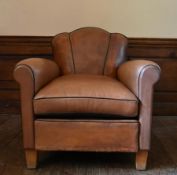A vintage club armchair in piped and studded tan leather upholstery on block supports. H.82 W.78 D.