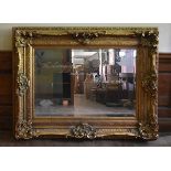 A gilt framed wall mirror in a heavy Rococo style frame, the bevelled plate with Oscar Wilde