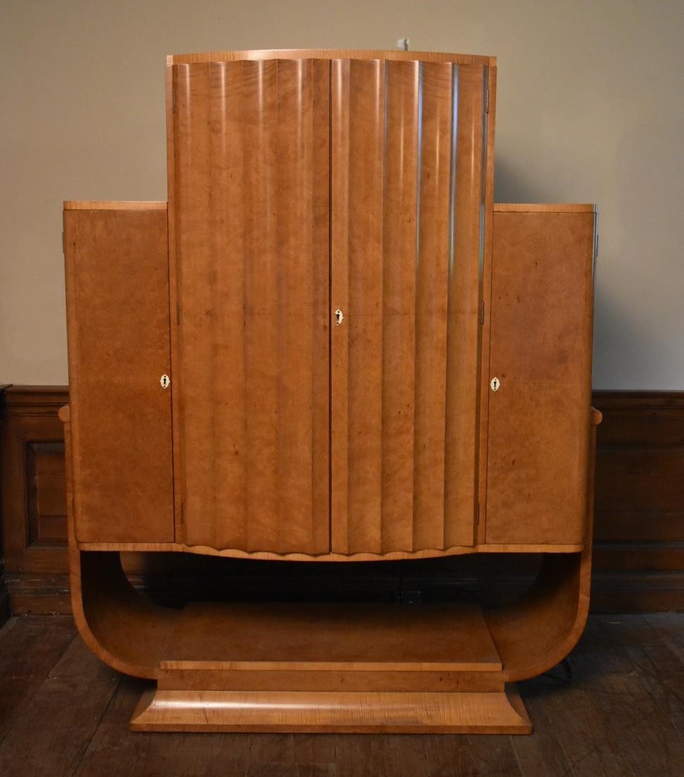 An Art Deco burr walnut cocktail cabinet with ribbed central panel doors enclosing glazed and lit