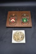 An embossed copper armorial plaque and a glazed tile depicting medieval wine making. H.25 W.33cm