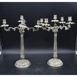 A pair of silver plated five branch table candelabras with palm decorated sconces on scrolling