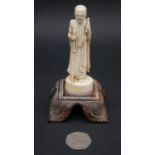An antique carved Chinese ivory statue of a Luohan mounted on a floral form hardwood base. H.13cm