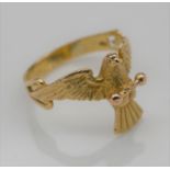 A yellow metal ring (tested 18 carat) in the form of a dove in flight holding a rose gold bar in its
