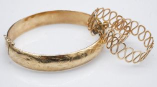 A yellow metal (tested as higher than 9ct gold) hollow engraved bangle with safety catch along