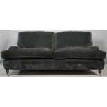 A two seater Howard style sofa in corded charcoal upholstery on turned supports terminating in brass