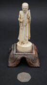 An antique carved Chinese ivory statue of a Luohan mounted on a floral form hardwood base. H.13cm