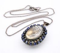 A white metal, sapphire and moonstone cluster pendant and chain. Set to centre with an oval cabochon