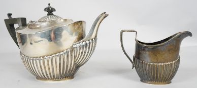 An Edwardian gadrooned silver tea pot and matching milk jug, with ebony finial and handle.