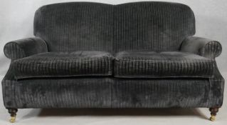 A two seater Howard style sofa in corded charcoal upholstery on turned supports terminating in brass