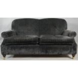 A two seater Howard style sofa in corded charcoal upholstery on turned supports terminating in brass