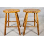 A pair of early 20th century elm seated stools on beech supports. H.53cm