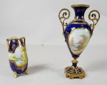 A twin handled hand painted landscape royal blue glaze vase with gilded scrolling detailing along