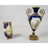 A twin handled hand painted landscape royal blue glaze vase with gilded scrolling detailing along