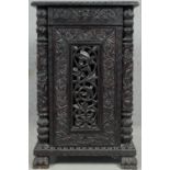 A Burmese hardwood cabinet with all over carved decoration and pierced panel door resting on paw