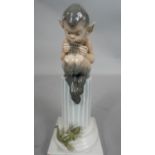 A Royal Copenhagen porcelain figure of a faun playing pan pipes seated on column with a lizard on