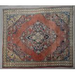 A Persian style rug with central floral medallion on a madder ground within naturalistic floral