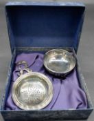 A boxed silver tea strainer and bowl. The bowl mounted on three lion paw feet and the handle of