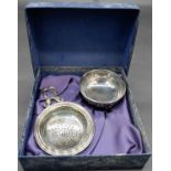 A boxed silver tea strainer and bowl. The bowl mounted on three lion paw feet and the handle of