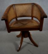 An Eastern teak revolving captains's desk chair with caned seat and back on swept quadruple