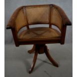 An Eastern teak revolving captains's desk chair with caned seat and back on swept quadruple