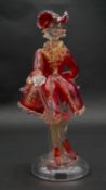A vintage Murano gold flecked red glass figure of a Venetian gentleman with cane, on a clear round