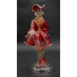 A vintage Murano gold flecked red glass figure of a Venetian gentleman with cane, on a clear round