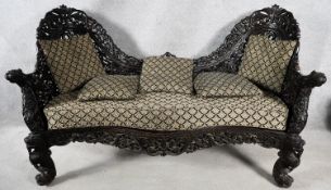 A Burmese hardwood double chair end chaise with all over carved and pierced decoration raised on