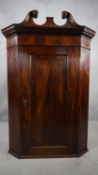 A Georgian flame mahogany corner cabinet with swan neck pediment above crossbanded door on plinth