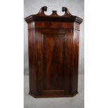 A Georgian flame mahogany corner cabinet with swan neck pediment above crossbanded door on plinth