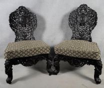 A pair of Burmese hardwood salon chairs with all over carved and pierced floral decoration raised on