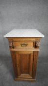 A late 19th century oak pedestal cabinet with marble top above frieze drawer and panel door