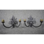 A pair of wrought aged iron Fleur-de-Lys design two branch Gothic style wall lights with brass