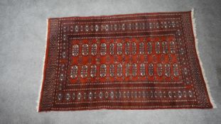 A Bokhara rug with rust ground elephants foot motifs within a repeated stylised border. H.92 W.148