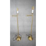 A pair of contemporary brushed brass swing arm height adjustable floor lamps with circular bases.