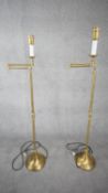 A pair of contemporary brushed brass swing arm height adjustable floor lamps with circular bases.