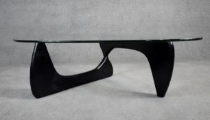 After Isamu Noguchi, a model IN-50 coffee table with plate glass top on folding ebonised base. H.