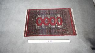 A signed Pakistan Bokhara rug with red ground within a central pendant motif. H.185 W.135