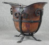 An Art Nouveau style copper helmet shaped coal bucket with wrought iron stand and hinged carrying