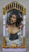 A plaster bust of Jesus Christ within a glass display case with gilded detailing and painted. H.84cm