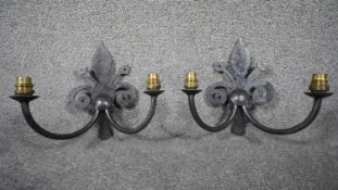 A pair of wrought aged iron Fleur-de-Lys design two branch Gothic style wall lights with brass