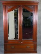 A late Victorian carved walnut wardrobe with twin shaped bevelled doors above base drawer on