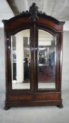 A C.1900 French burr walnut armoire with arched carved pediment above twin shaped and bevelled doors