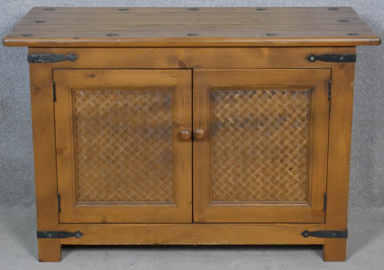 An Eastern teak brass bound side cabinet with rattan panelled doors on block feet. H.62 W.95 D.47.