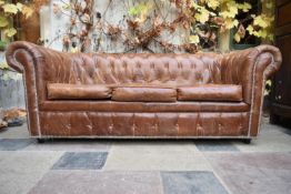 A three seater Chesterfield sofa in deep buttoned and studded tan leather upholstery. H.77 W.197 D.