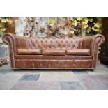 A three seater Chesterfield sofa in deep buttoned and studded tan leather upholstery. H.77 W.197 D.