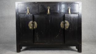 A Chinese black lacquered side cabinet with three frieze drawers above panel doors on block feet.