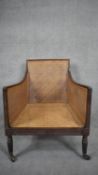 A Regency mahogany framed bergere tub library chair with caned back and seat raised on reeded